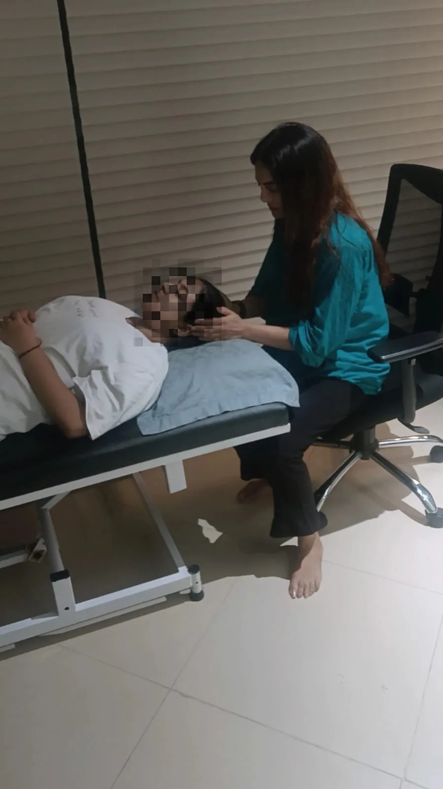 A hypnotherapy session in progress with a client resting comfortably and the therapist seated alongside. The client's identity has been obscured for privacy.